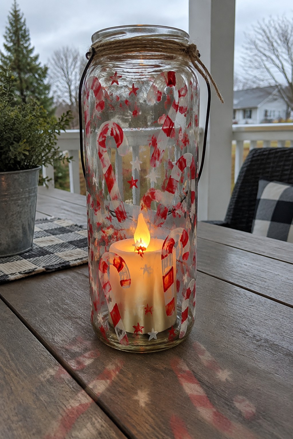 Lit candle inside glass jar painted with red candy canes and stars on wooden table