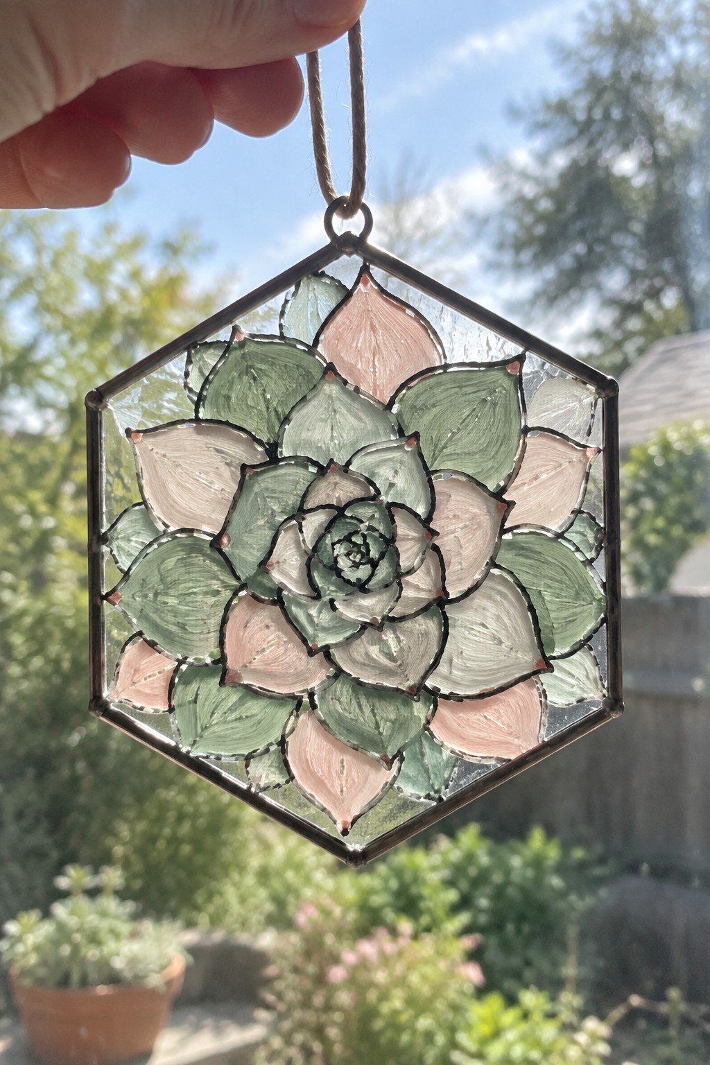 Hand holding hexagonal stained glass succulent ornament in green and pink hues.