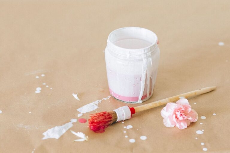 Small glass jar being painted beside a red paintbrush on messy kraft paper