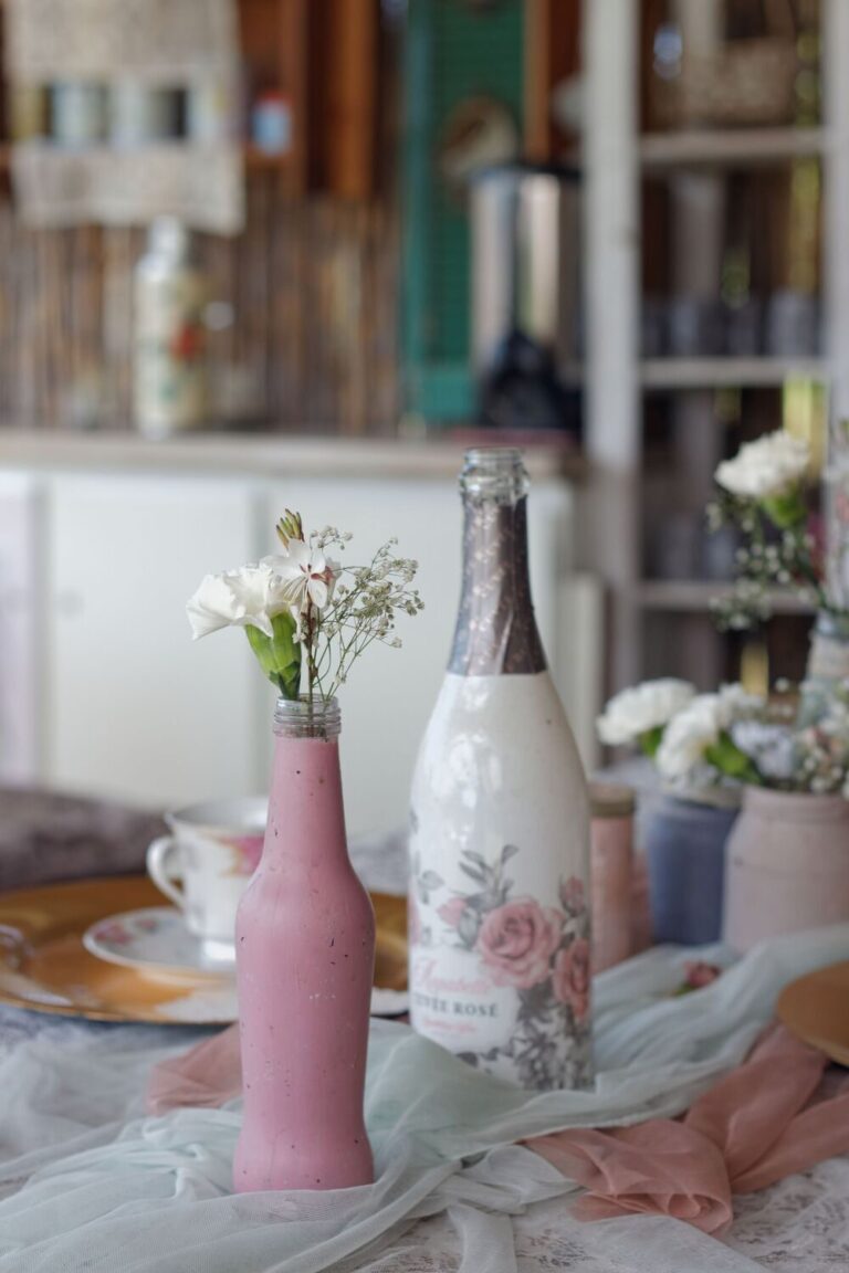 Handmade painted glass bottles used as flower vases on a lace-covered table