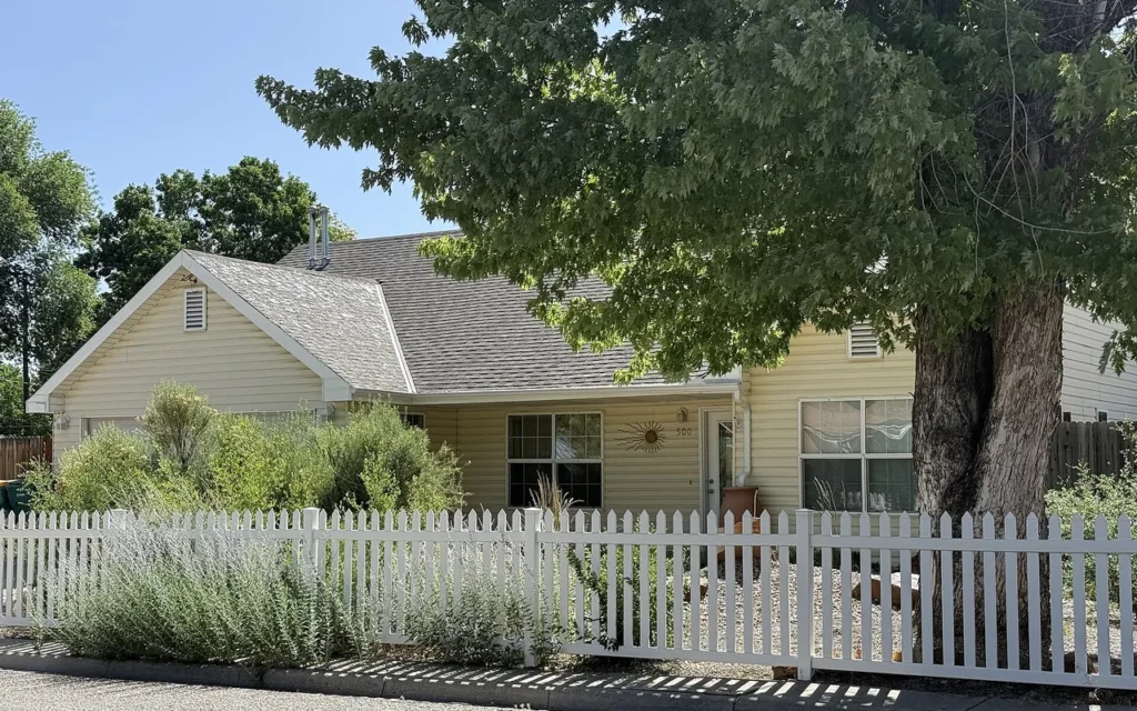 A house with a white picket fence and a large shade tree in the front yard