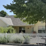 A house with a white picket fence and a large shade tree in the front yard